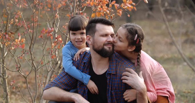 Portrait of father with two daughters in beautiful autumn forest. Bearded man in plaid shirt  hugging little girls, smiling, having fun looking to camera. Father's day concept. 50 fps slow motion 4k