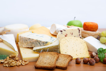 Heap of different cheeses and snacks set. Slices of bread, fruits and nuts on brown wooden table. Closeup, copy space. Gourmet or rustic food concept