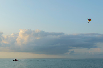 Parasailing flight. A parachute with man being towed at sea with a boat. Water amusement in the sea during holidays. Blue sky with a large cloud in the background with copyspace.