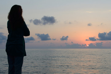 Fototapeta premium Profile of woman silhouette standing and watching sea sunset. Tranquil lady meditation on the sea during sunset. Yoga practicing on the beach during sundown