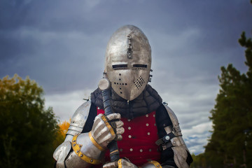Knight in helmet and red brigantine against the background of thunderclouds. With a two-handed sword in his hands. 
