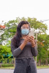 Young Indian woman with mask and face shield using phone at the park outdoors