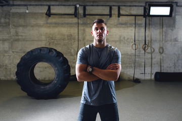 Serious muscular man in sportswear standing with arms crossed in cross-fit gym.