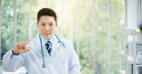 Professional Asian doctor portrait wearing stethoscope medical and holding vaccine liquid bottle in modern office with green bokeh background. Copy space available