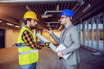 Angry caucasian businessman in suit and helmet on head arguing with irresponsible construction...