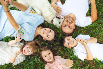 Happy beautiful big family together mother, father, children and dog lying on the grass top view