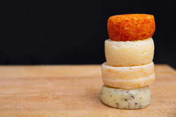Stack of whole spicy cheeses on wooden table against dark wall background. Closeup, side view, copy space. Cheese dairy advertising concept