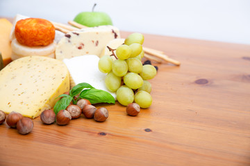 Spicy cheeses and snacks set. Apples, bunch of grapes and nuts on brown wooden table. Closeup, copy space. Gourmet or rustic food concept