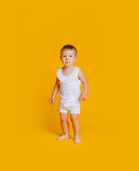 Fototapeta na wymiar Little boy stands in a white T-shirt and underpants on an orange-yellow background