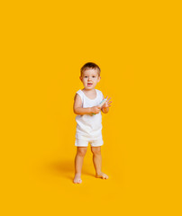 A little boy is standing in a white T-shirt and underpants and with a comb in his hands on an orange-yellow background