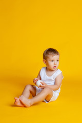 little boy in a t-shirt and underpants on an orange-yellow background with a white Christmas ball in his hands
