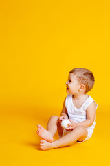 little boy in a t-shirt and underpants on an orange-yellow background with a white Christmas ball in his hands