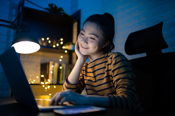 Asian woman happy smiling working on a laptop at the night at home. WFH. Work from home avoid COVID...