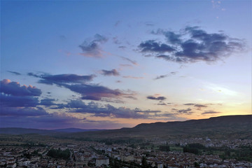 Beautiful sunrise in the valley of Cappadocia. In the distance, the sun rises from behind the mountain. The sky is colored by rays in golden, orange, pink tones. The clouds are blue and lilac.