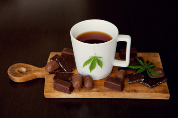 Marijuana green leaves in cup of tea on wooden background. Chocolate marijuana sweets. Delicious...