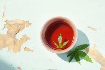 Marijuana leaf in cup of tea on blue wooden background. Medical marijuana. Concept of herbal alternative medicine, cbd oil, pharmaceptical industry, growing cannabis indoors. Copy space
