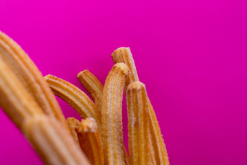 Churros with sugar in paper bag on pink background