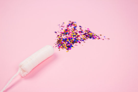 Clean cotton tampon with colorful sparkles on pink background with copyspace - critical days and menstruation concept. Flat lay composition for Menstrual Hygiene Day concept