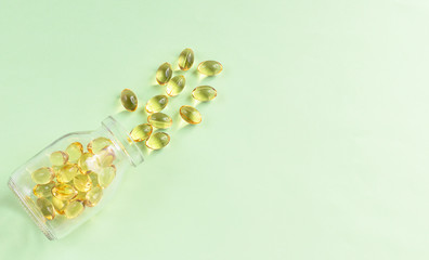 Yellow omega-3 capsules from a glass bottle on a green background. Copyspace for text. Health care, natural, natural supplements. Lifestyle concept