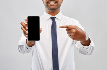 business, technology and people concept - close up of smiling indian businessman showing black smartphone screen over grey background