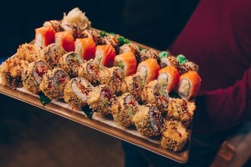 Close-up Hand Waiter holding Set Delicious fresh Sushi slate plate, Japanese raw fish Warm Ebi Sake Unagi . Philadelphia flesh Rolls served on plate in sushi bar.  Japan food menu service