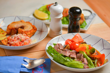 Salad with meat and vegetables. Italian cuisine, different dishes served in restaurant on light rustic wooden table.
