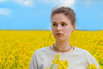  Brunette girl in rapeseed field  summer time, looking a side blue sky background.  Happy beautiful...
