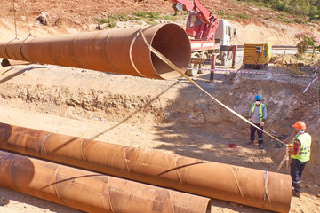 Workers are laying metal culverts under the highway under construction