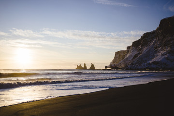 Schwarzer Strand in Island mit Felsen und Berge bei Sonnenuntergang