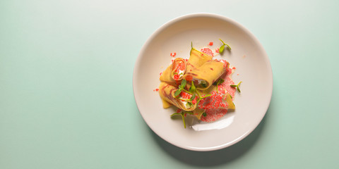 Crepes stuffed with cream cheese and salmon with sour cream sauce and red caviar over pastel blue mint background.