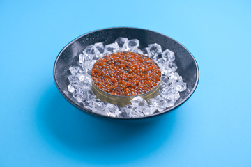Bowl of red caviar on vintage black metal tray with ice over bright blue background. Top view, copy space, flat lay.