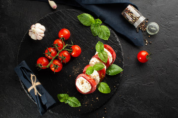 Mozzarella,fresh tomatoes,basil leaves,garlic and spices on stone plate with kitchen towel.Caprese salad top view.