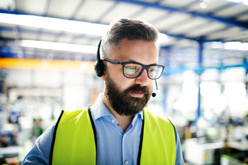 Front view of technician or engineer with headset standing in industrial factory.