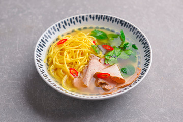 Japanese ramen soup with noodles, beef, egg, fresh parsley and sweet pepper on gray background. Copy space banner.