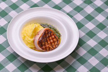 Filet mignon with mashed potatoes and pesto sauce served in a white plate over green plaid tablecloth. Beef steak.
