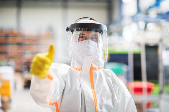 Worker with protective mask and suit in industrial factory, thumb up hand gesture.