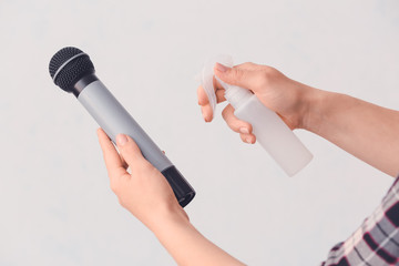 Woman disinfecting microphone on grey background