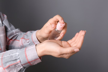 Woman using sanitizer on grey background