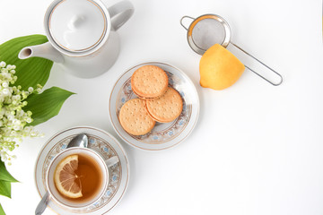 Porcelain tea set with a cup, teapot on white tablecloth with cookies on a plate and lilies of the valley on table. Afternoon tea party concept. Breakfast. Morning. Home sweet home.