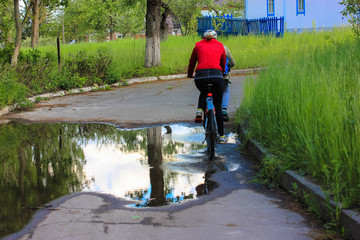 Woman riding bicycle on a road and giant puddle on the tarmac after the rain