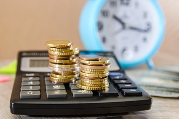 Stacks of coins on a calculator with an alarm clock in the background. Tax concept. Money saving...