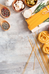 Different uncooked pasta and spices on grey background