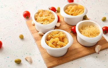 Different uncooked pasta with vegetables on white background