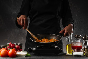 Chef fries vegetables in a pan, carrots and onions. Against the background of vegetables. Cooking and gastronomy. Home recipe book.