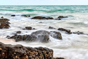 a wavy sea with rocks near a beach.