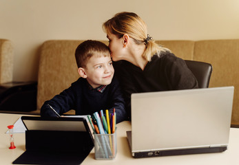 Mother using laptop and tablet teaching with her son online at home in his room