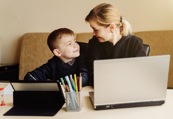 Mother using laptop and tablet teaching with her son online at home in his room