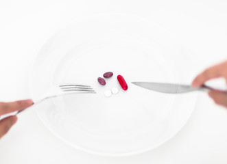 Diet and medication concept. Persons point of view of eating colorful pills on a plate with fork and knife. 