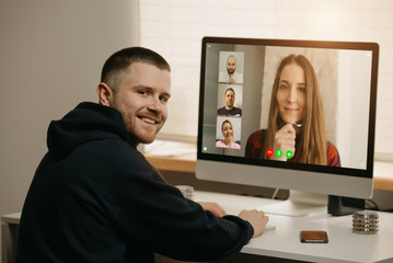 Remote work. A back view of a man during a video call with his colleagues on the desktop computer. A fellow distracted and smiles from an online briefing at home.