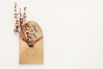 Greeting card with text Mom We love you! in craft envelope with heart and bouquet of spring branches and flowers. International Mother's day, birthday, eco concept. Minimalism